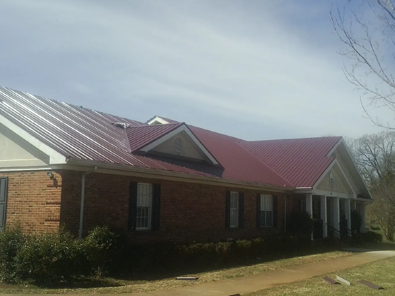 Red metal roof with gabled entries on a long brick building, from a Hail Damage Roof Repair job in Naples